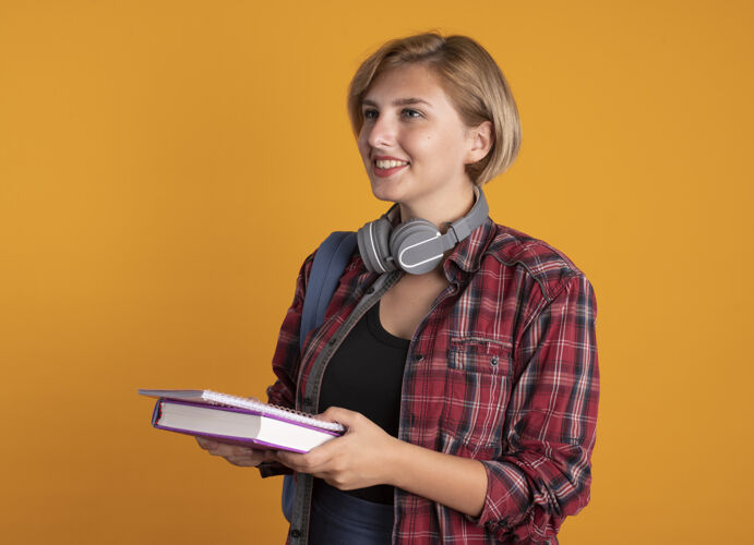 背包微笑的年轻斯拉夫女学生戴着耳机背着书包拿着书和笔记本耳机笔记本斯拉夫