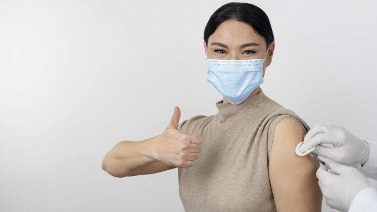 安全带着医用口罩的女病人在注射疫苗时竖起大拇指治疗面罩预防