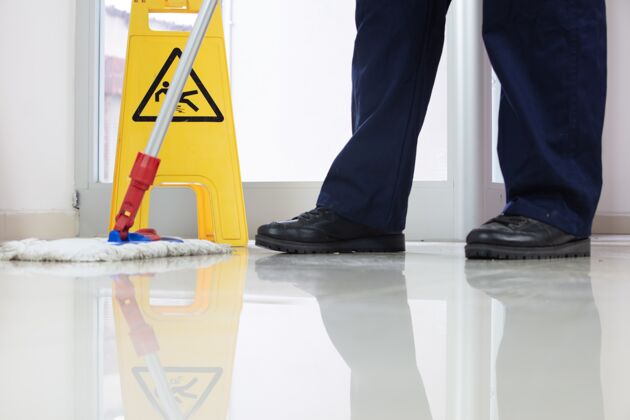 人员低角度特写一个人用拖把清洁地板附近的黄色警告湿地板标志安全地板警告