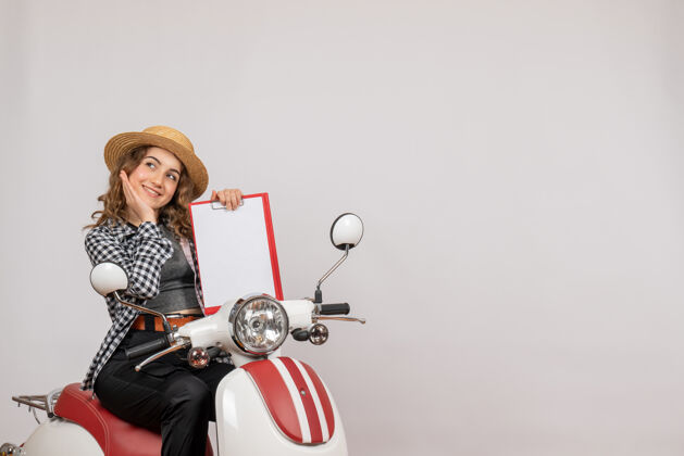 摩托车坐在轻便摩托车上微笑的旅行女孩拿着红色的剪贴板腾出空间红色坐车辆