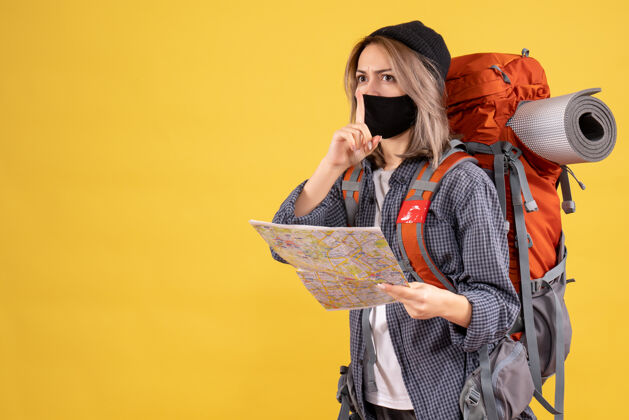 人带着黑色面具和背包的旅行女孩拿着地图做着安静的标志安静肖像面具