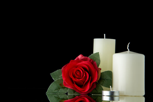 爱黑墙上有红花的白色蜡烛的正面图玫瑰葬礼黑