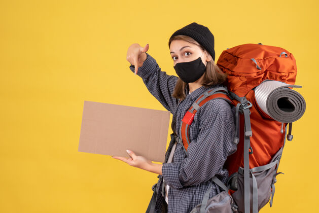 脸带着黑色面具和背包的旅行女孩指着纸板纸板女孩旅行者肖像
