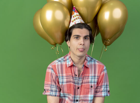 生日自信英俊的白种人戴着生日帽 跺着舌头站在氦气球前站立穿空间