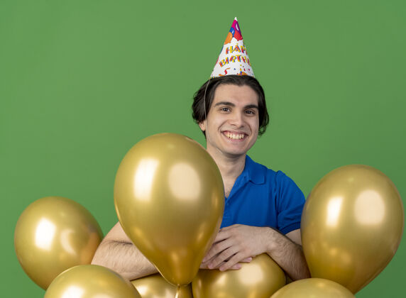 穿微笑英俊的白人男子戴着生日帽站在氦气球站立空间帽子
