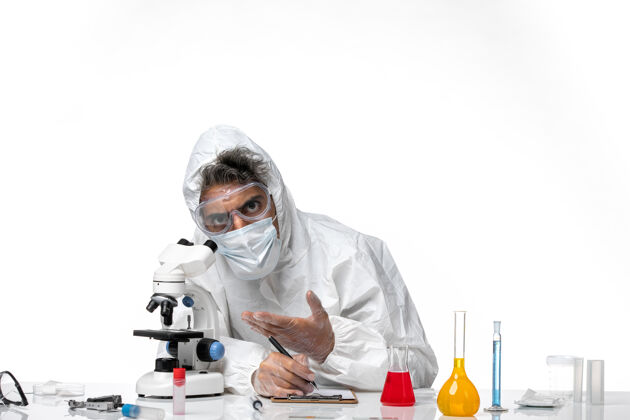 笔记穿防护服的男医生写下笔记 用显微镜观察白色医生实验室病毒