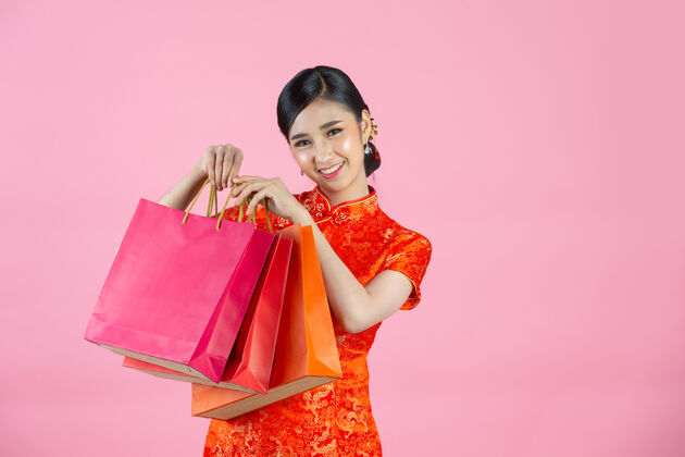 红色美丽的亚洲女人快乐的微笑和购物在中国新年的粉红色背景亚洲问候语服饰