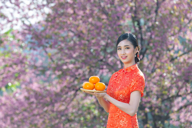 展示美丽的亚洲女人开心地微笑着 手里拿着粉红背景的新鲜橘子过年文化亚洲东方