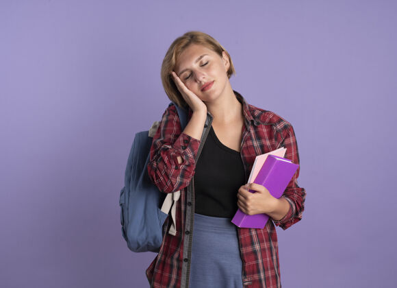紫色高兴的年轻斯拉夫学生女孩戴着背包把手放在脸上拿着书和笔记本女孩复制年轻