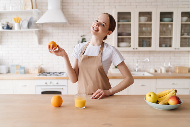 室内年轻漂亮的女人在厨房里围着围裙 水果和橙汁微笑自然健康