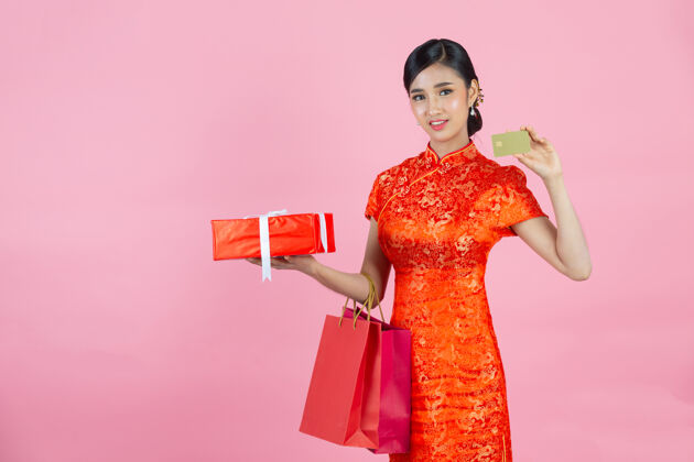 衣服美丽的亚洲女人开心的微笑 在粉色背景上展示中国新年的信用卡礼物复制空间女孩