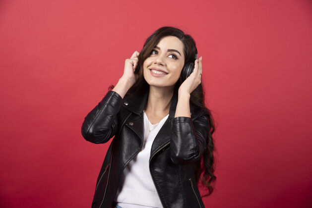 人类戴着耳机听音乐 在红色背景上摆姿势的年轻女子高质量照片女性女孩手持
