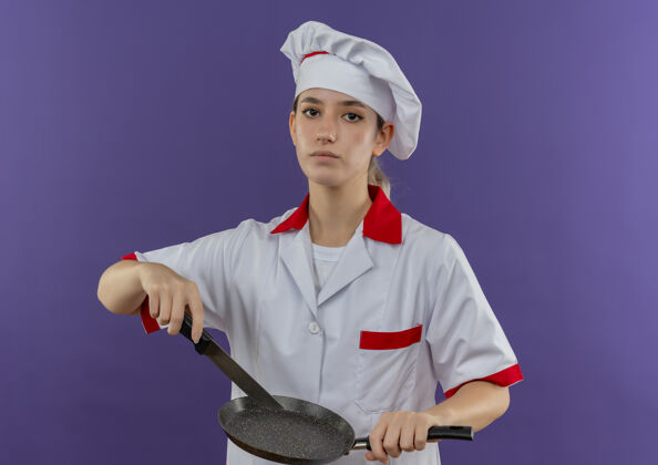锅自信的年轻漂亮厨师 身着厨师制服 手里拿着煎锅和刀 隔离在紫色的墙上年轻制服信心