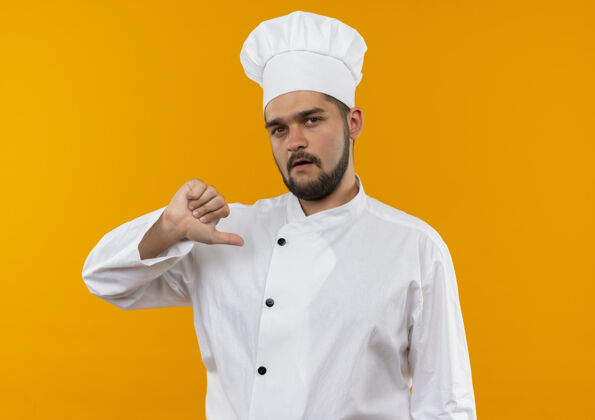 自己身着厨师制服的自信的年轻男厨师指着隔离在橙色墙上的自己厨师制服自信