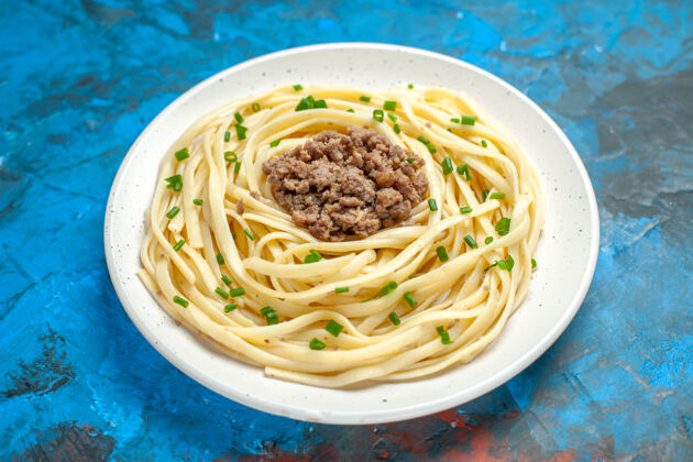 肉前视图美味的意大利面食与绿色和磨碎的肉在蓝色面团上一餐菜的颜色盘子意大利面磨碎的
