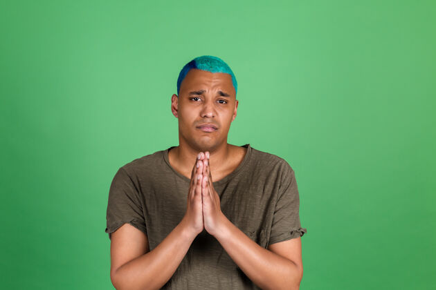 男性年轻人在随意的绿墙上蓝头发一起祈祷双手坏站立害怕