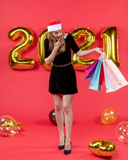成人正面图：穿着黑色连衣裙的年轻女士拿着购物袋 红色的气球气球包姿势