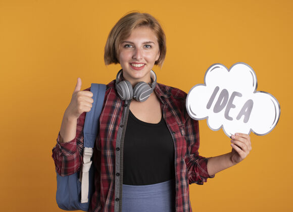 穿微笑着的年轻斯拉夫女学生戴着耳机 背着背包 举着创意泡泡大拇指背包创意斯拉夫