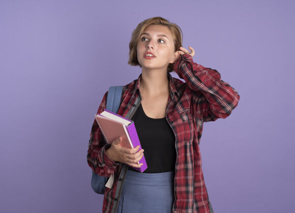 信心自信的年轻斯拉夫女学生背着书包拿着书和笔记本看着身边紫色斯拉夫背包