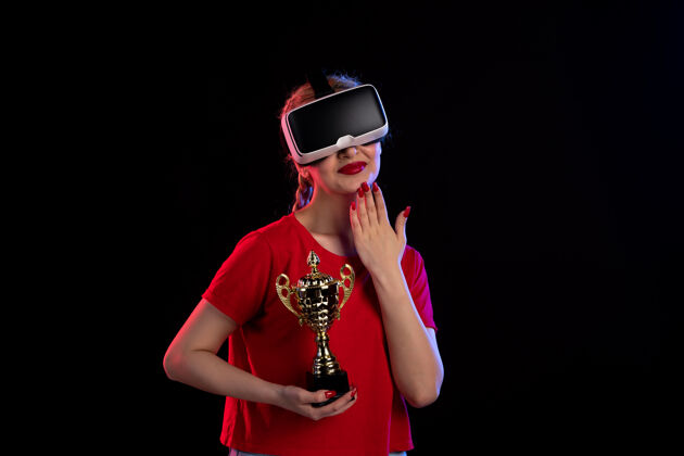 虚拟现实在黑暗的墙壁上 年轻女性正在玩虚拟现实和冠军杯正面视图杯子