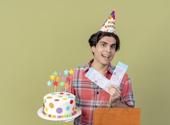 帅哥快乐英俊的高加索男子戴着生日帽 手里拿着纸购物袋 机票和生日蛋糕机票生日帽子