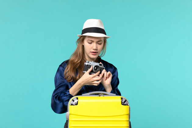 航行前视图年轻女子拿着相机 试图把它固定在蓝色背景女子海上旅行飞机肖像尝试旅行