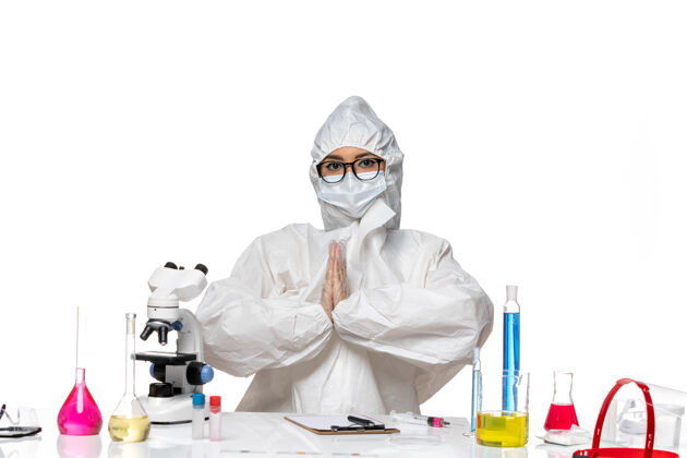 坐姿正面图穿着特殊防护服的年轻女化学家正坐在桌子前 用白色背景病毒的溶液对实验室的covid健康化学化学药品实验室