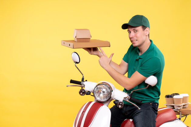 摩托车正面图身着制服的年轻男性快递员手持黄色食品包装运输机货箱工作
