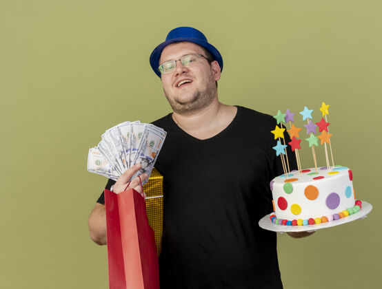 礼物高兴的成年斯拉夫男子戴着眼镜 戴着蓝色派对帽 手里拿着钱礼盒 纸购物袋和生日蛋糕购物男人生日