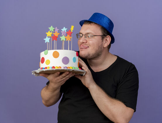 复制兴奋的成年斯拉夫人戴着眼镜 戴着蓝色派对帽 跺着舌头 拿着生日蛋糕聚会紫色眼镜