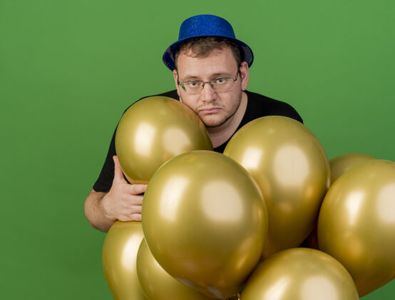 男人心烦意乱的成年斯拉夫人戴着眼镜戴着蓝色派对帽拿着氦气球绿色斯拉夫举行