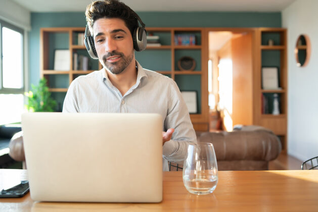 职业年轻人在家里用笔记本电脑进行工作视频通话的肖像家庭办公室概念新的正常生活方式房子专业耳机
