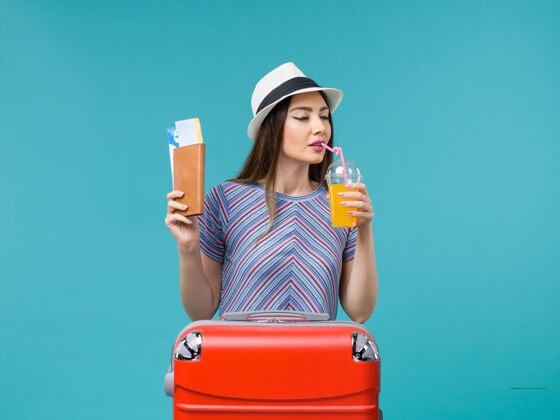 休闲前景度假的女人拿着新鲜的果汁和蓝色背景的机票旅行度假海上夏天旅行人举行