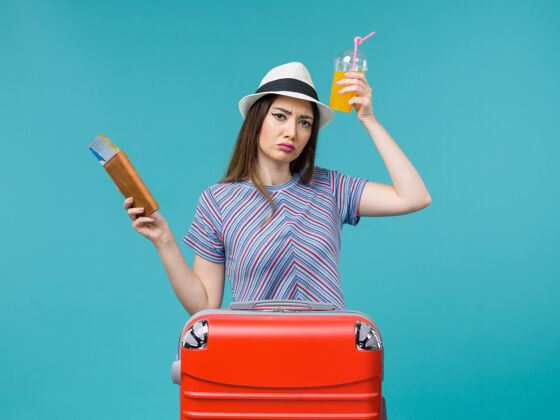 果汁前景：度假的女人拿着新鲜的果汁和蓝色背景的机票旅行度假海上避暑美丽肖像票