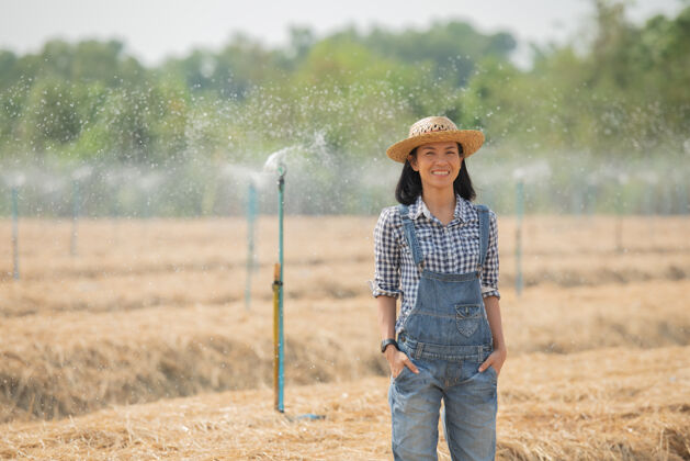 人亚洲年轻的女农民戴着帽子站在田里 走在田里的妇女来视察农业园植物生长概念生态 运输 清洁空气 食品 生物制品微笑有机农场