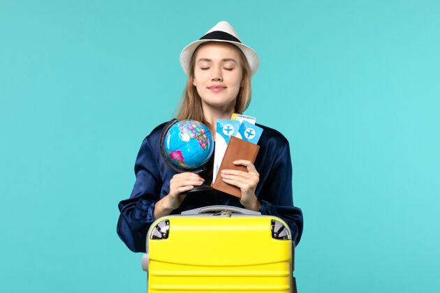 小正面图年轻女子手持机票和蓝色背景飞机上的小地球仪女性度假旅行远航大海肖像举行票