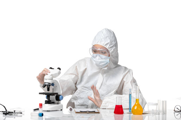 面罩正面图年轻女医生穿着白色防护服 戴着口罩 由于科维德在显微镜下工作 背景为浅白色病毒大流行 飞溅科维德-人显微镜医生