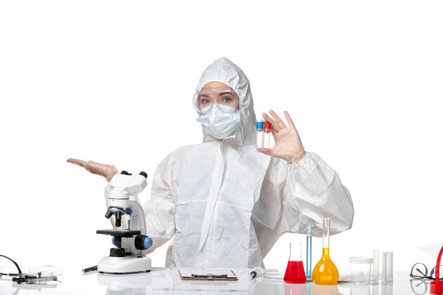 外套正面图年轻女医生穿着白色防护服 戴着口罩 因为柯维德在白色办公桌上拿着烧瓶大流行性飞溅病毒健康柯维德-烧瓶实验室外套病毒