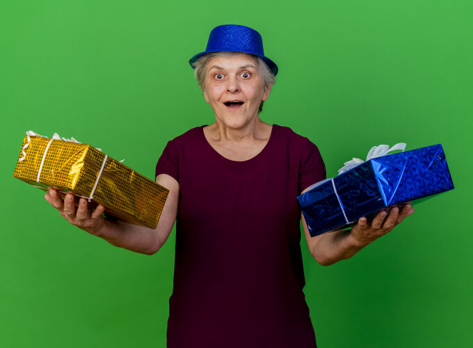 盒子一位戴着派对礼帽的惊讶的老妇人拿着礼品盒站在草地上老人礼物惊喜