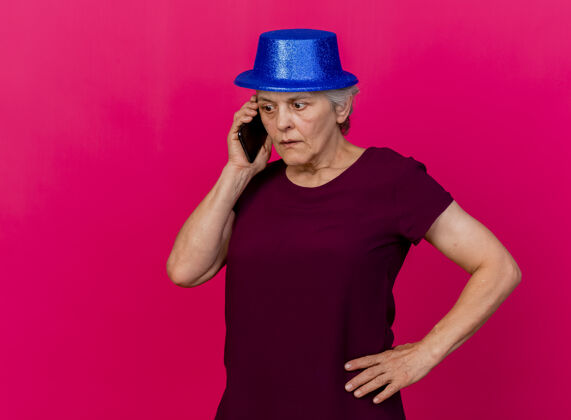 老人惊讶的老太太戴着聚会帽把手放在腰上打电话穿粉红色帽子手派对