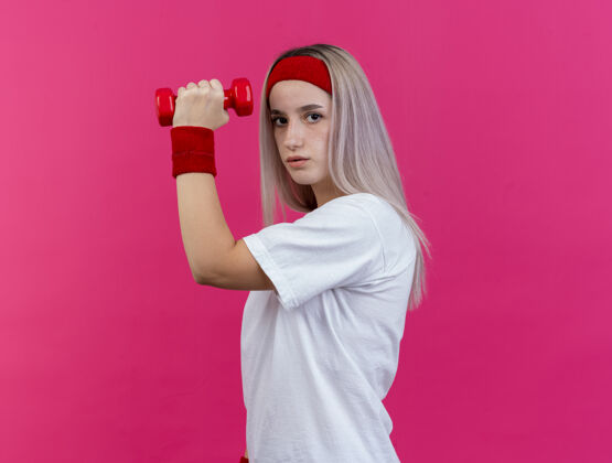 头带自信的年轻白人运动女孩戴着背带和头带哑铃站立背带