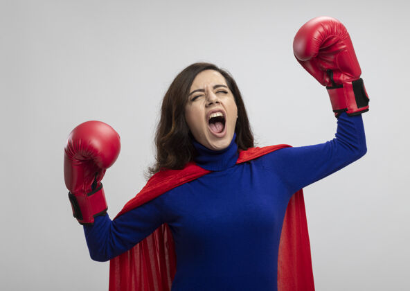 手愤怒的高加索超级英雄女孩身穿红色斗篷 戴着拳击手套 举手站立超级英雄愤怒站起来