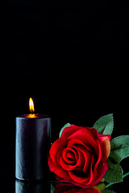 烛光黑暗表面上有红玫瑰的黑暗蜡烛的正视图燃烧前面火