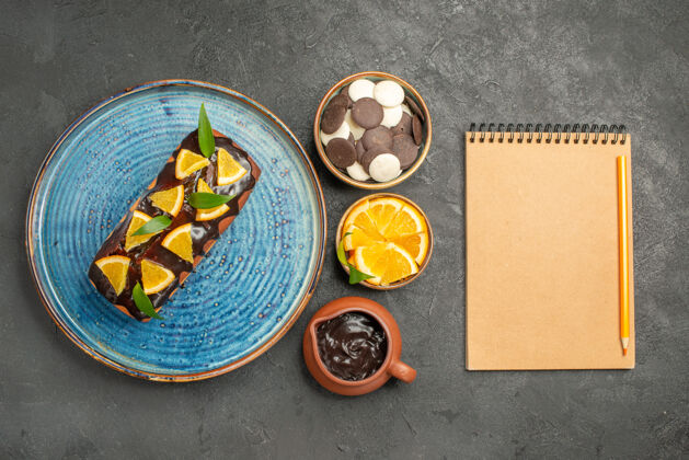 帽子黑色桌子上装饰着柠檬和巧克力的美味蛋糕和笔记本的垂直视图柠檬黑色容器