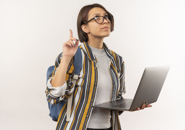 脸体贴的年轻女学生戴着眼镜 背着包拿着笔记本电脑 孤零零地指着白色的墙上背人拿着
