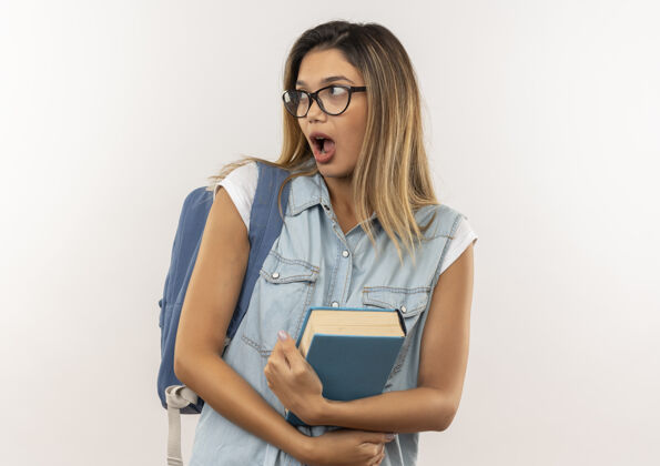 年轻惊讶的年轻漂亮的女学生戴着眼镜 背着书包 看着隔离在白墙上的一面人背部人