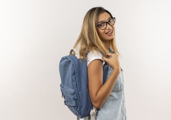 人微笑着的年轻漂亮的女学生戴着眼镜 背着书包站在侧视图上 看着隔离在白色墙上的前面站立微笑年轻