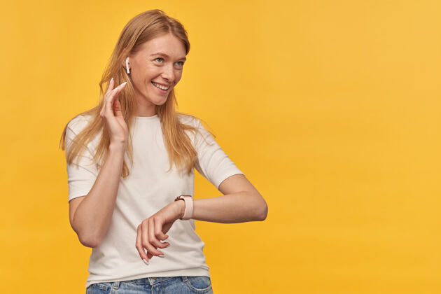 年轻快乐美丽的女人 带着雀斑 穿着白色T恤 戴着无线耳机听音乐 戴着黄色智能手表金发耳机请