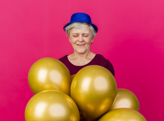 粉色高兴的老妇人戴着聚会帽站在粉红色的氦气球上老人站着氦气