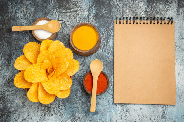 美味美味的薯片装饰成花朵形状的不同香料 上面放着勺子 灰色的桌子上放着笔记本笔记本花瓣健康